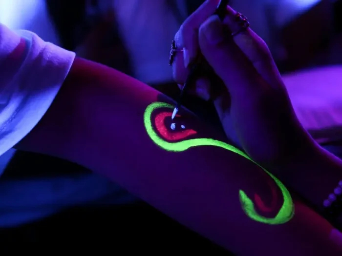 Close-up of fluorescent body paint being applied under blacklight.